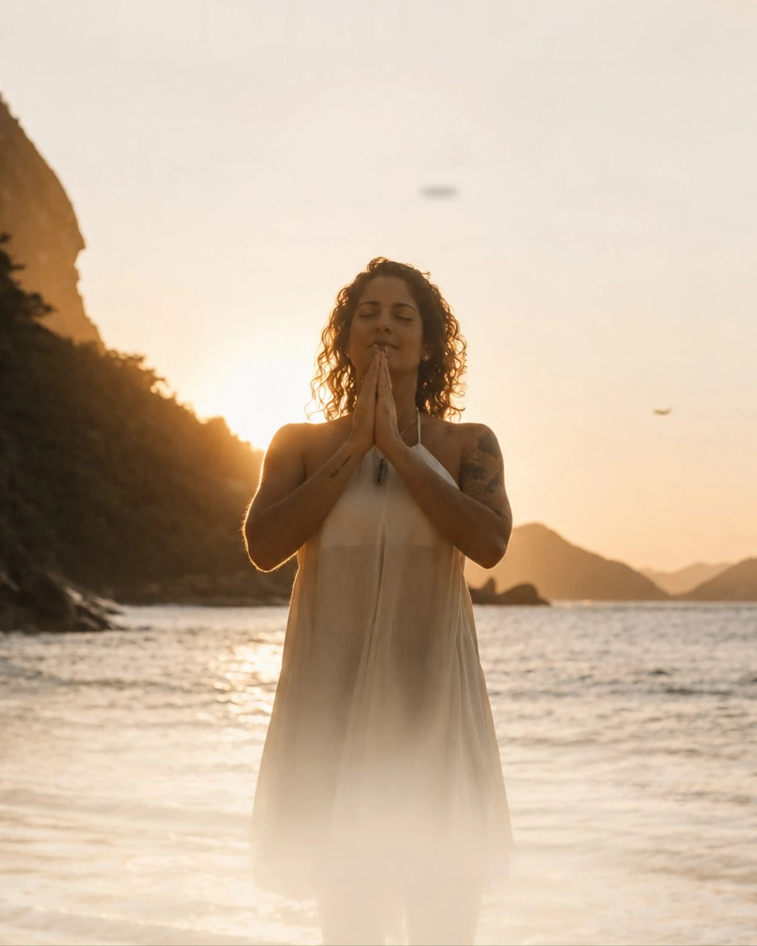 Mulher meditando à beira-mar ao pôr do sol
